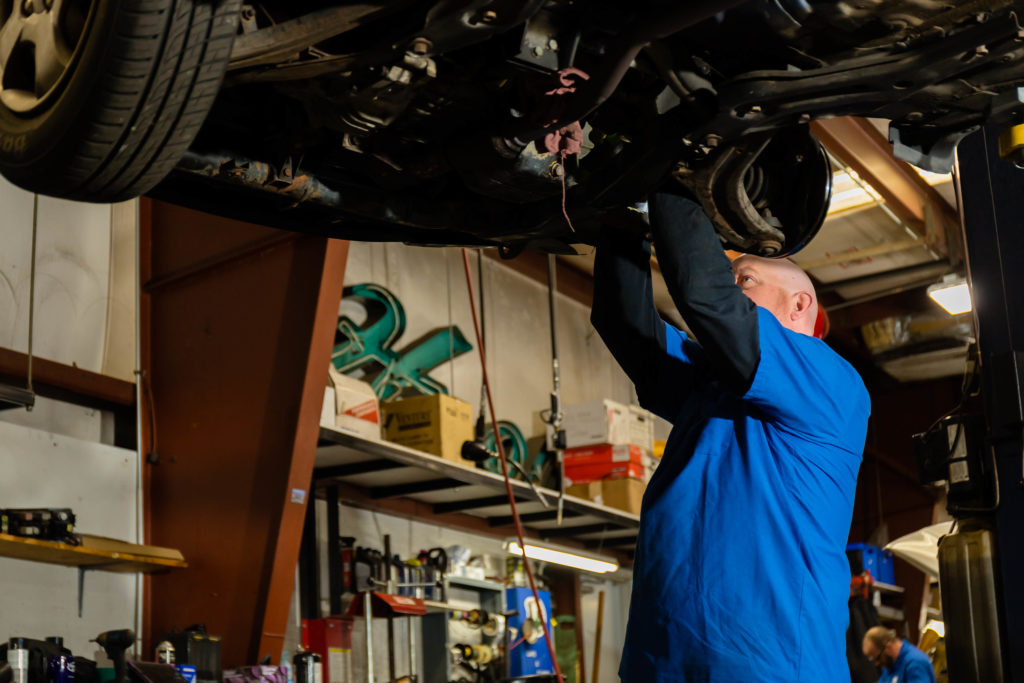 Honest Accurate technician inspects mounted vehicle to determine if auto suspension repairs are needed.