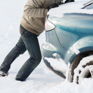 A person attempts to push a car out of the snow