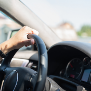 One hand on a steering wheel as a car drives.