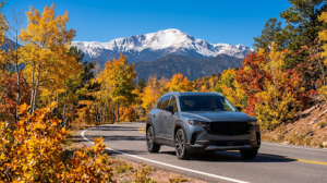 A modern SUV driving on a mountain road surrounded by golden fall foliage with snow-dusted Pikes Peak in Colorado Springs