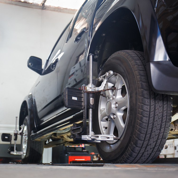 Close-up of a rear tire on a black car in an auto shop. Car is in the middle of a wheel alignment with equipment attached.